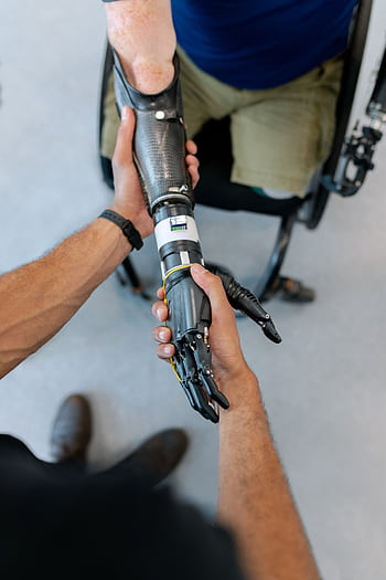Close-up of a man in a wheelchair with a prosthetic hand offering a handshake. HD phone wallpaper
