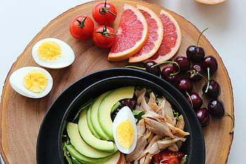 A vibrant, healthy salad bowl with avocado, eggs, tomatoes, grapefruit, and cherries on a wooden board. HD wallpaper