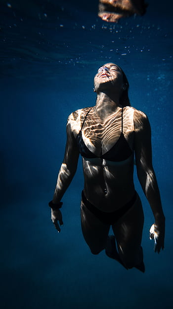 Serene underwater shot of a woman enjoying a swim in a resort pool. HD phone wallpaper