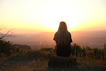 Woman sitting in nature, watching sunset over fields. Peaceful and serene outdoor scene. HD wallpaper