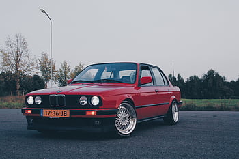 Classic red BMW E30 parked outdoors, showcasing its vintage style and chrome features. HD wallpaper