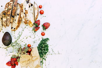 A flat lay of fresh ingredients including bread, strawberries, and avocado on marble. Perfect for food and lifestyle ry. HD wallpaper