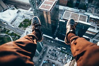 Exhilarating rooftop view of cityscape below with legs dangling from edge. HD wallpaper