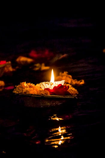 A close-up of a candle with flowers on water during a spiritual festival, creating a serene ambiance. HD phone wallpaper