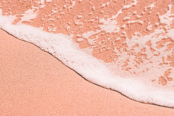 Close-up of a pink sandy beach as gentle sea foam encroaches on the shore, creating a tranquil coastal scene. HD wallpaper
