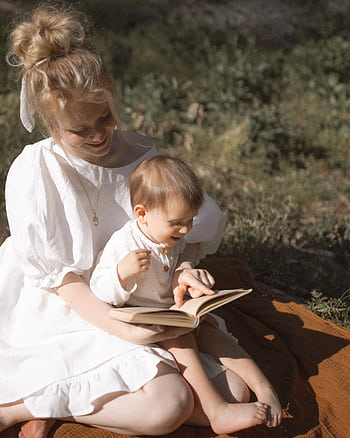 A mother and toddler enjoy reading together in a sunny outdoor setting. HD phone wallpaper