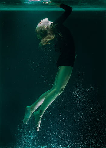 Elegant underwater shot of a woman floating in a serene pose, captured in dim turquoise light. HD phone wallpaper