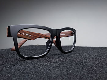 Close-up of fashionable black and wooden frame glasses on dark fabric with a soft-focus background. HD wallpaper