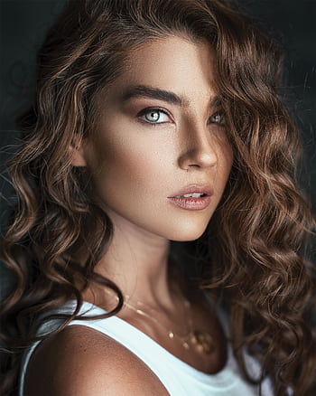 Captivating portrait of a woman with curly hair and striking eyes posing in natural light. HD phone wallpaper