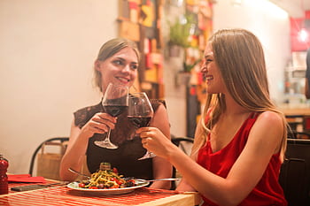 Two women sharing a joyful moment over dinner and wine at a cozy restaurant. HD wallpaper