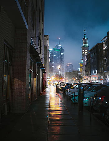 A captivating view of the Indianapolis skyline with parked cars and illuminated streets at night. HD phone wallpaper