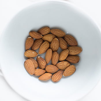 A close-up view of organic almonds in a white bowl, ideal for healthy snacking. HD phone wallpaper
