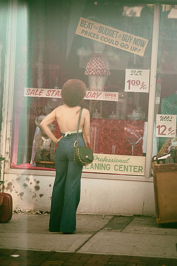 A woman in retro fashion standing outside a vintage store with sale signs in NYC. HD phone wallpaper