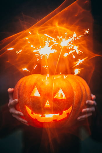 Glowing Halloween pumpkin with sparklers creating an eerie effect. HD phone wallpaper