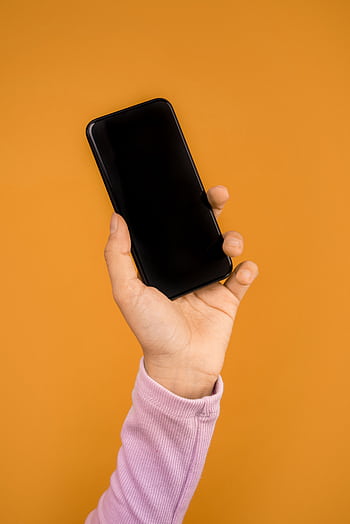 Close-up of a hand holding a smart against a bright orange backdrop, emphasizing modern technology. HD phone wallpaper