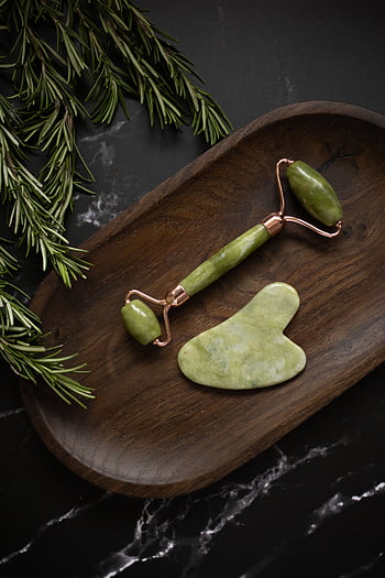 A top-down view of a jade roller and gua sha on a dark wooden tray, surrounded by rosemary. HD phone wallpaper
