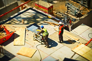 Construction workers engaging in tasks at an outdoor building site with safety hats and equipment. HD wallpaper