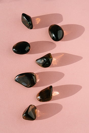 Arrangement of black gemstones casting shadows on a pink background, perfect for zen and relaxation themes. HD phone wallpaper