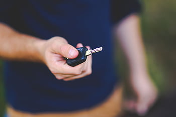A hand holding a car key outdoors, emphasizing security and control. HD wallpaper