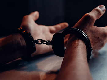A close-up of human hands handcuffed on a table with a dark background, depicting law enforcement themes. HD wallpaper