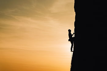 A silhouette of a rock climber scaling a steep cliff during sunset in Russia, showcasing determination and adventure. HD wallpaper