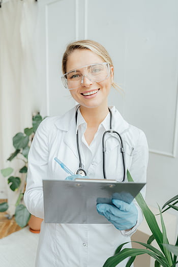 Confident female doctor with clipboard in a bright medical office. HD phone wallpaper