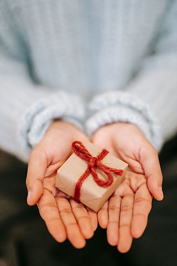 Close-up of hands offering a small gift wrapped with a red bow, ideal for festive occasions. HD phone wallpaper