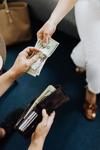 Close-up of hands exchanging cash, representing a financial transaction or payment. HD phone wallpaper