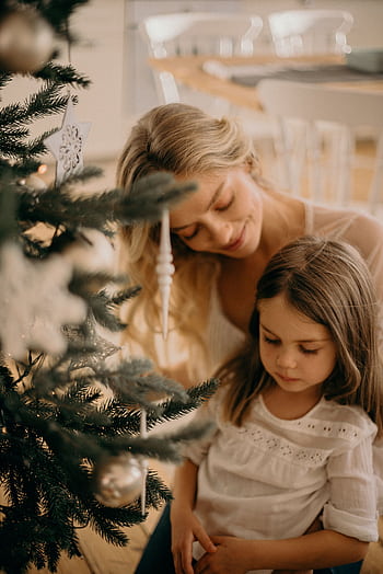 A mother and daughter enjoy decorating a Christmas tree at home, capturing warmth and holiday spirit. HD phone wallpaper
