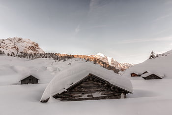 Tranquil cabins nestled among snow-covered alpine slopes during a peaceful winter dawn. HD wallpaper