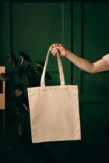 Simple cotton tote bag held by a hand against a green background, ideal for eco themes. HD phone wallpaper