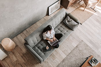 High angle view of a woman working on a laptop while sitting on a sofa in a modern living room. HD wallpaper