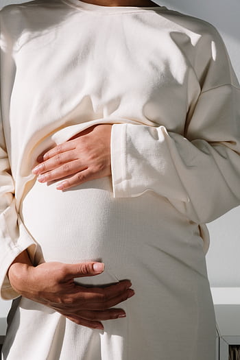 A serene close-up of a pregnant woman cradling her belly, bathed in warm sunlight. HD phone wallpaper