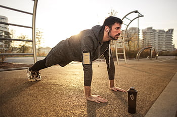 Adult man doing push-ups outdoors with ears during sunrise, showcasing fitness and healthy lifestyle. HD wallpaper