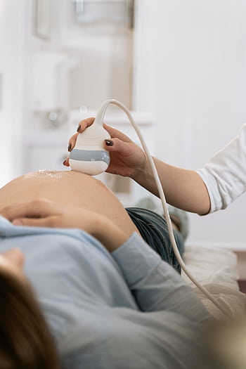 A pregnant woman undergoing a medical ultrasound in a clinical setting. HD phone wallpaper