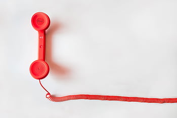 Vintage red handset with coiled cable on a clean white background, classic communication device. HD wallpaper