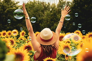A joyful woman in a sunflower field with bubbles, expressing happiness on a summer day. HD wallpaper