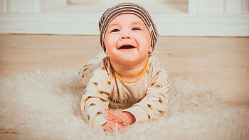 Smiley Cute Baby Boy Is Lying Down On White Fur Cloth Wearing Yellow White Dress And Cap Cute HD wallpaper