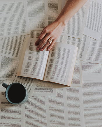 A hand reaching over an open book surrounded by pages with a coffee cup nearby, creating a cozy reading scene. HD phone wallpaper