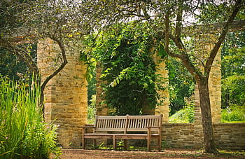 A tranquil park bench set under a stone archway surrounded by lush greenery and trees. HD wallpaper