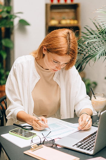 Woman analyzing financial documents using laptop and calculator indoors. HD phone wallpaper