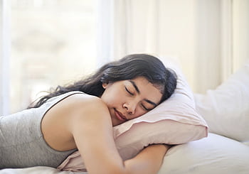 Serene woman resting on a comfortable bed with soft pillows and natural light. HD wallpaper