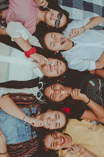 Joyful group of diverse women enjoying a sunny picnic with lollipops, showcasing friendship and fun. HD phone wallpaper