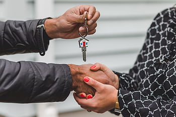Close-up of a realtor handing over a house key to a new homeowner, symbolizing ownership and investment. HD wallpaper