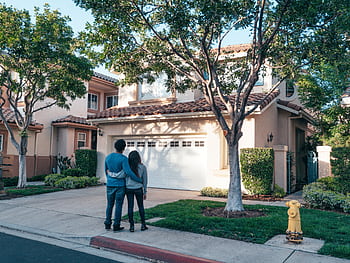 Couple hugging outside their newly purchased suburban home, showcasing togetherness and new beginnings. HD wallpaper