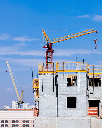 Tower cranes at a construction site working on a high-rise building under a clear blue sky. HD phone wallpaper