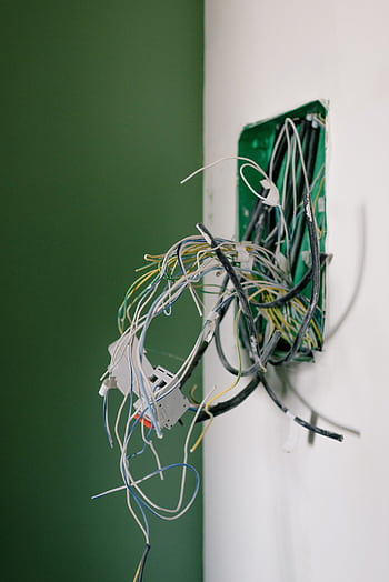 Close-up of exposed electrical wires in a wall socket, ideal for illustrating renovation or repair concepts. HD phone wallpaper
