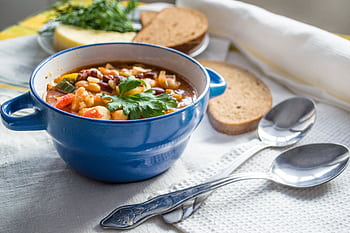 Colorful vegetable soup served in a blue ceramic bowl with bread slices on a cozy table setting. HD wallpaper