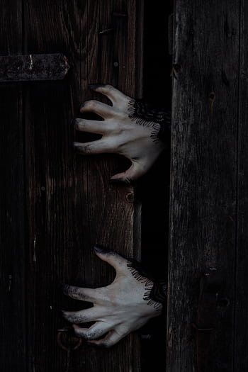 Eerie white hands with black nails reach through a dark wooden door, perfect for Halloween themes. HD phone wallpaper
