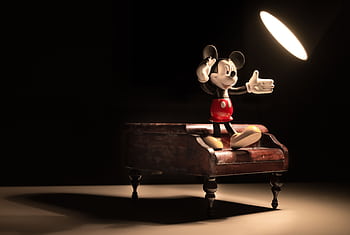 Mickey Mouse figurine poses on a wooden miniature piano under a spotlight. HD wallpaper